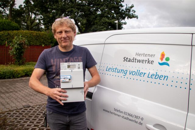 Thomas Knels steht neben einem Stadtwerke-Fahrzeug und hält einen smarten Stromzähler in die Kamera.