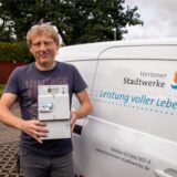 Thomas Knels steht neben einem Stadtwerke-Fahrzeug und hält einen smarten Stromzähler in die Kamera.