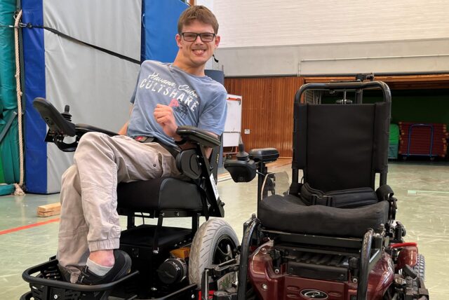 Till Martenka (32) in seinem neuen Powerchair neben dem alten Powerchair. Das alte Modell fällt mittlerweile fast auseinander, es gibt keine Ersatzteile mehr und die Technik ist veraltet.