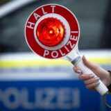 Eine Polizistin hält während einer Verkehrskontrolle eine Polizeikelle mit der Aufschrift ·Halt Polizei· hoch.