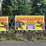 An einem Jägerzaun an der Hubertusstraße in Recklinghausen hängen Plakate für die Veranstaltung Dinosaurier – Im Land der Giganten.