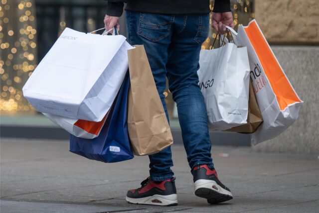 Mit vollen Einkaufstüten in den Händen geht ein Mann am verkaufsoffenen Sonntag durch eine Einkaufsstraße.