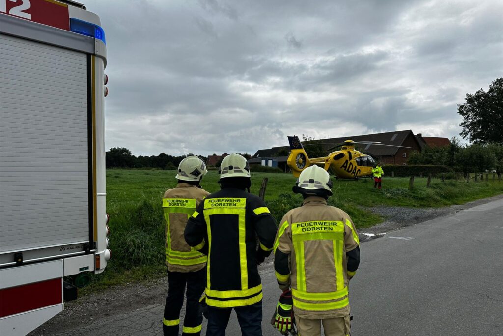 Drei Feuerwehrmänner stehen auf einer Straße und sichern die Landung eines Rettungshubschraubers ab. Drei Feuerwehrmänner stehen auf einer Straße und sichern die Landung eines Rettungshubschraubers ab.