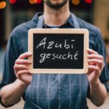 Jemand hält ein Schild hoch, auf dem steht „Azubis gesucht“.