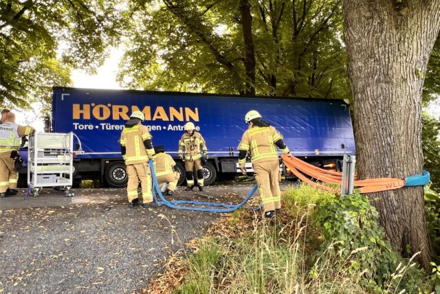 Vier Feuerwehrmänner sichern einen in einen Graben an der Lindenstraße gerutschten Lkw im Stadtteil Speckhorn in Recklinghausen mit einer um einen Baum geschlungenen Seilwinde gegen ein Umkippen.