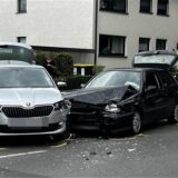Zwei Autos stehen nach einem Unfall auf einer Straße. Rechts ist ein Feuerwehrmann zu sehen. Ein schwarzes Auto hat schweren Schaden davongetragen.