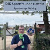Redakteur Uwe Wallkötter steht vor einer Sportanlage in Datteln. Er hält ein Mikrofon in der Hand.