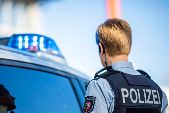 Eine Polizistin steht vor einem Streifenwagen, dessen Blaulicht leuchtet.