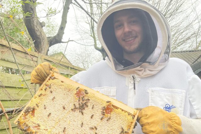 Micky Cassano hält eine Honigwabe mit Bienen darauf in die Kamera.