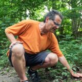 Recklinghäuser Ralf Nickel hockt im Wald und berührt ein Stück Rinde auf dem Boden.