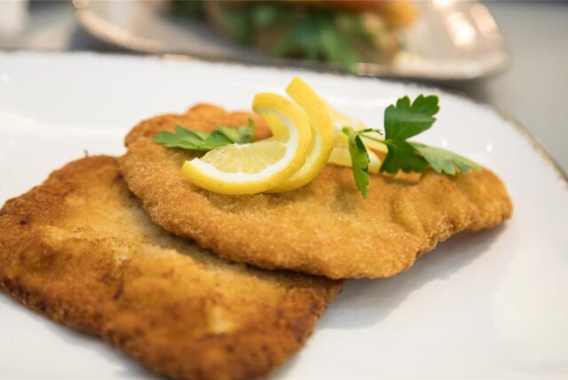 Ein Schnitzel mit Zitronenscheiben darauf auf einem Teller.