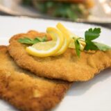 Ein Schnitzel mit Zitronenscheiben darauf auf einem Teller.