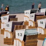 Menschen gehen am Samstag bei warmem, sonnigen Wetter an verschlossenen Strandkörben am Ostseestrand vorbei.
