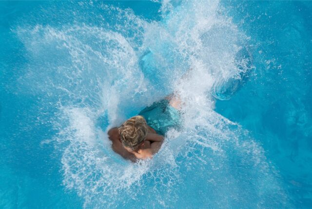 Ein Junge springt im Freibad vom 5-Meter-Turm ins Wasser (Archivbild).
