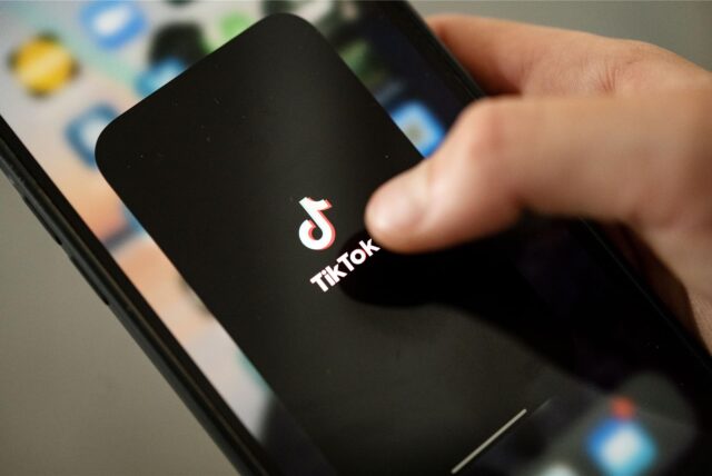 Ein Teenager tippt auf das TikTok-Logo auf einem Smartphone.