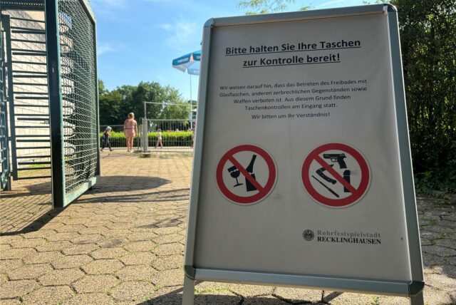 An jedem der drei Freibäder in Recklinghausen hat die Stadt Recklinghausen diese Klappaufsteller aufgestellt, auf denen steht: Bitte halten Sie Ihre Taschen zur Kontrolle bereit! Dazu befinden sich zwei Verbotsschilder auf dem Aufsteller: Eins zeigt durchgestrichen ein zerbrochenes Glas und eine zerbrochene Flasche. Das zweite zeigt durchgestrichen eine Pistole, ein Pfefferspray, ein Klappmesser und einen Teleskopschlagstock. Im Hintergrund ist der Eingangsbereich des Südbads samt Drehkreuz zu e