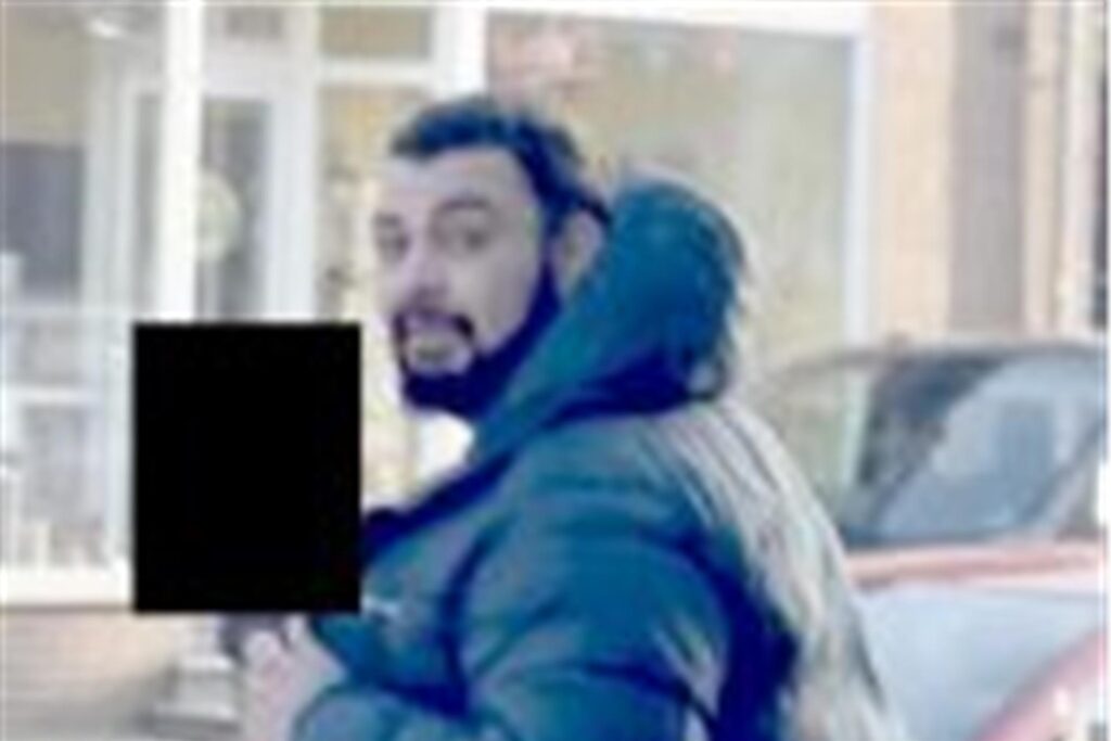 Ein Mann, bekleidet mit einer schwarzen Winterjacke und einer Cargohose, geht über eine Straße. Ein Mann, bekleidet mit einer schwarzen Winterjacke und einer Cargohose, geht über eine Straße.