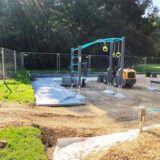 Blick auf die Baustelle, auf der der neue Fitnessparcours im Backumer Tal in Herten entsteht. Zwischen den Sportgeräten steht ein kleiner Bagger.