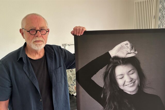 Fotograf Peter Knauf steht neben einem seiner Ausstellungsstücke, auf dem eine Frau mit geschlossenen Augen lächelt.