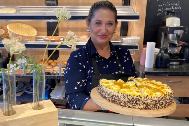 Aida Suvalic steht in ihrem Café Kulisse hinter der Theke und hält einen Obstkuchen in den Händen.