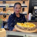 Aida Suvalic steht in ihrem Café Kulisse hinter der Theke und hält einen Obstkuchen in den Händen.