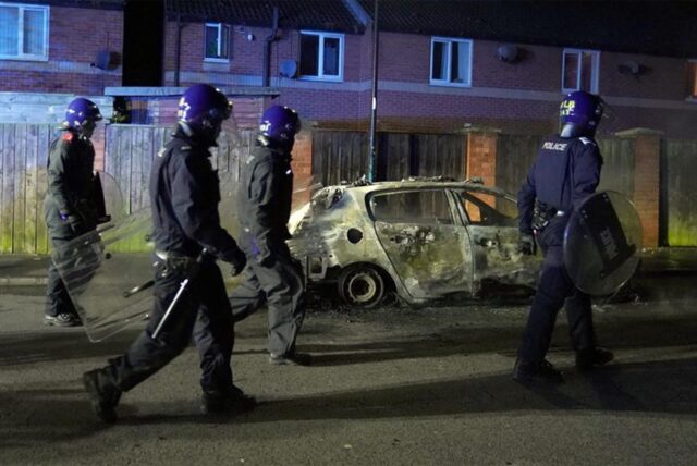 Polizeibeamte gehen an einem ausgebrannten Polizeifahrzeug vorbei, als sie nach einem gewalttätigen Protest in den Straßen von Hartlepool eingesetzt werden. Nach dem tödlichen Messerangriff im britischen Southport kam es auch in der nordostenglischen Stadt Hartlepool zu Zusammenstößen.