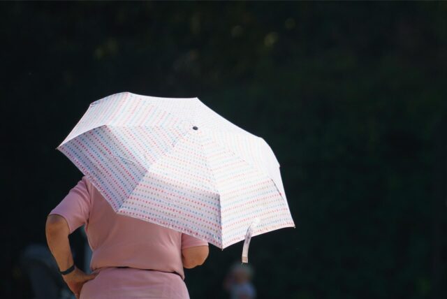 Eine Frau steht mit aufgespanntem Regenschirm in der Sonne.