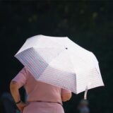 Eine Frau steht mit aufgespanntem Regenschirm in der Sonne.