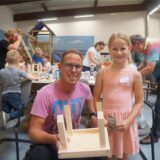 Ein Vater, mit seiner Tochter, hält ein Holzhaus in der Hand.