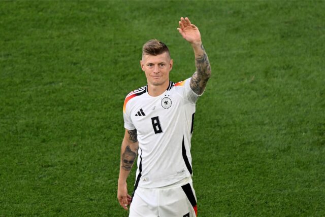 Fußballer Toni Kroos winkt auf dem Spielfeld im weißen Trikot der Deutschen Nationalmannschaft.
