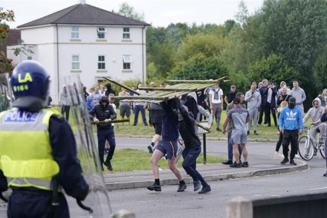 Jugendliche Randalierer werfen einen Teil eines Zauns auf die Polizei während einer Demonstration gegen Einwanderung in der Nähe des Holiday Inn Express Hotel, in dem Asylbewerber untergebracht sind.