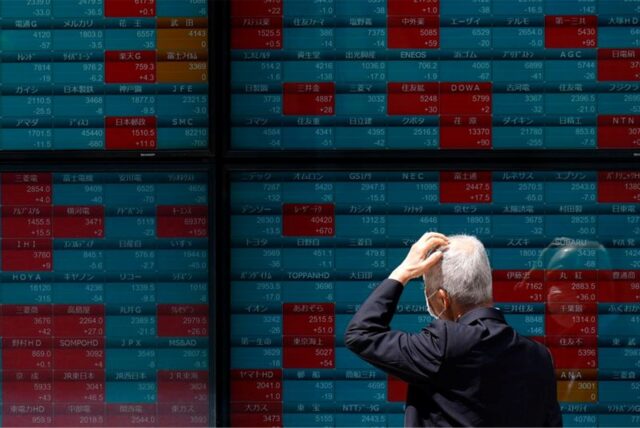 Eine Person blickt auf eine elektronische Anzeigentafel in einer Wertpapierfirma, die Börsenkurse des japanischen Nikkei-225-Index anzeigt.