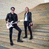 Musiker Ernest und Autorin Pia Lüddecke stehen auf einer großen Treppe.