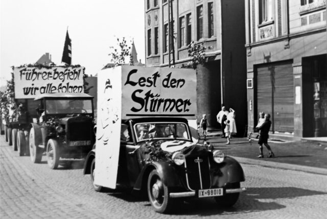 Ein historisches Foto zeigt einen Propagandazug durch Datteln. Zwei Frauen und ein Mann halten ein Plakat hoch.