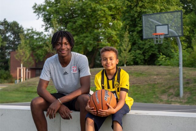 Ein Jugendlicher und ein Kind, die an einem Basketballfeld sitzen.
