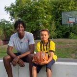 Ein Jugendlicher und ein Kind, die an einem Basketballfeld sitzen.