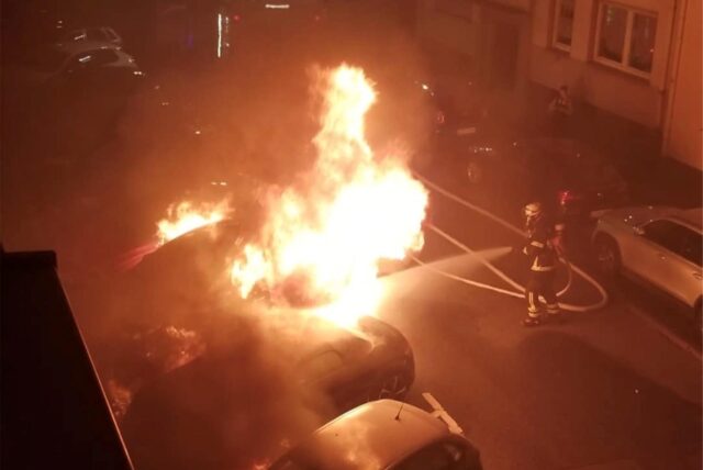 Ein Auto in Dortmund steht in Flammen, ein Feuerwehrmann versucht es zu löschen