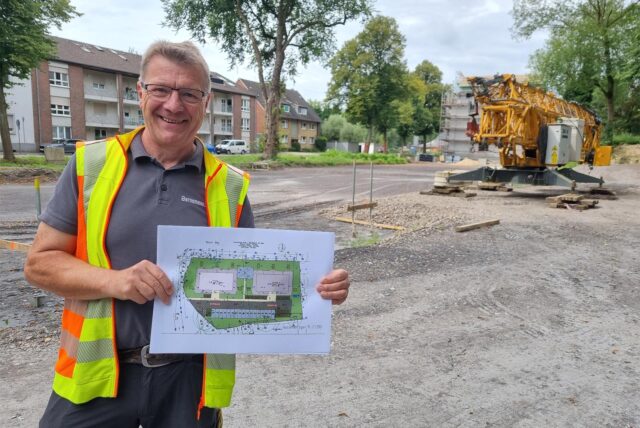 Thomas Bernemann steht an einer Baustelle und hält einen Plan hoch.