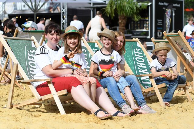 Zwei Frauen sitzen mit Kindern in Liegestühlen auf Sand.