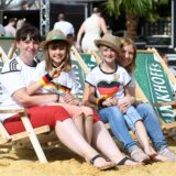 Zwei Frauen sitzen mit Kindern in Liegestühlen auf Sand.