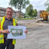 Thomas Bernemann steht an einer Baustelle und hält einen Plan hoch.