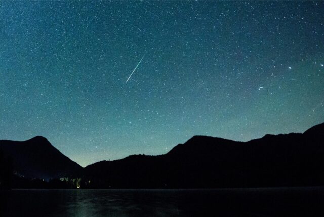 Eine Sternschnuppe leuchtet neben der Milchstraße am Himmel.