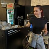 Niki Pasha steht an der Kaffee-Maschine an der Bar des Hertener Lokals BarOlo. Im Hintergrund ist ein Kühlschrank mit Getränken zu sehen.