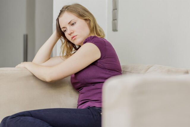 Eine Frau sitzt nachdenklich auf einem Sofa.