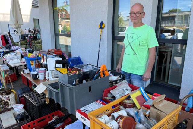 Stefan Schlitz steht vor einem Tisch mit Werkzeugen, Baumaterialien und Trödel.