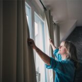 Eine Frau zieht Vorhänge zu.