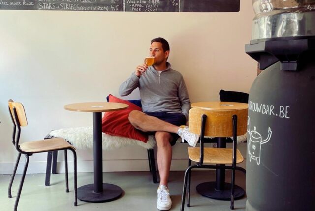 Ein Mann sitzt mit überkreuzten Beinen am Tisch und genießt ein Craft Beer.