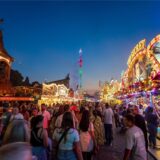 Eine große Menschenmenge läuft über die Cranger Kirmes. Die Sonne ist untergegangen. An den Seiten stehen zahlreiche Stände.