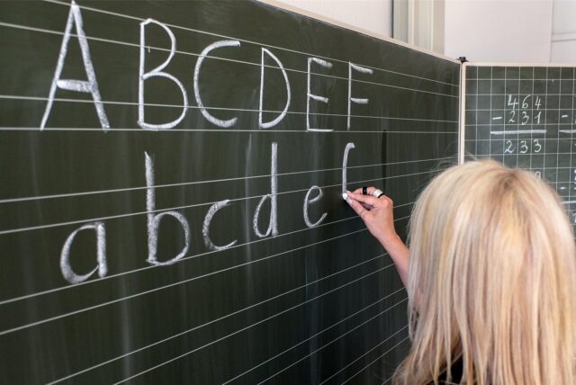 Eine Lehrerin schreibt Buchstaben an die Tafel.