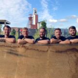 Fünf Männer haben ihre Arme auf eine Holzbohle gestützt. Im Bild-Hintergrund ist die Zeche Schlägel und Eisen in Herten-Langenbochum zu sehen.